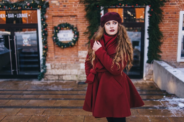 Mooi meisje dat een rode laag en een baret op Kerstmisstraat draagt