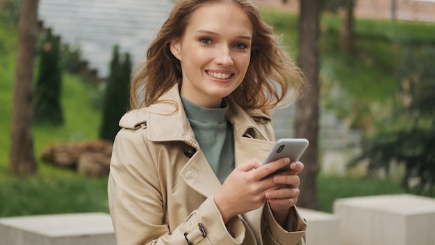 Mooi meisje dat er blij uitziet bij het controleren van sociale netwerken op smartphone buiten Positieve vrouwelijke student die in het stadspark rust