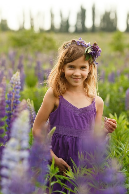 Mooi meisje dat in een violette kleding met een kroon van lupines glimlacht