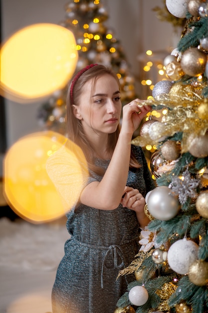 Mooi meisje dat Kerstboom verfraait. een jonge glimlachende vrouw bereidt een kerstboom voor op de vakantie. Weelderige groene kerstboom met gouden ballen