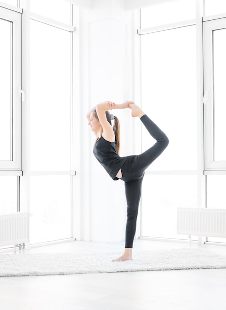 Mooi meisje dat koningsdanser yoga-asana binnenshuis uitvoert