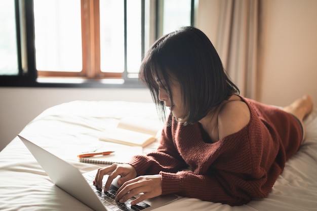 Mooi meisje dat met laptop op het bed werkt, werk vanuit huis concept