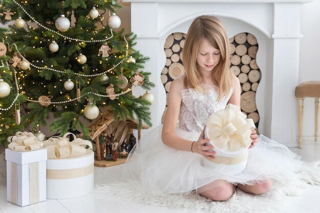 Mooi meisje dat naast de kerstboom zit om cadeaus te openen
