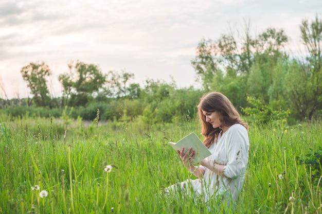 Mooi meisje dat op gebied een boek leest. het meisje, zittend op een gras, een boek lezen. rust en lees