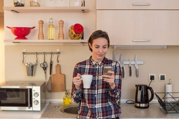 Mooi meisje dat van koffie geniet en mobiele telefoon met behulp van.