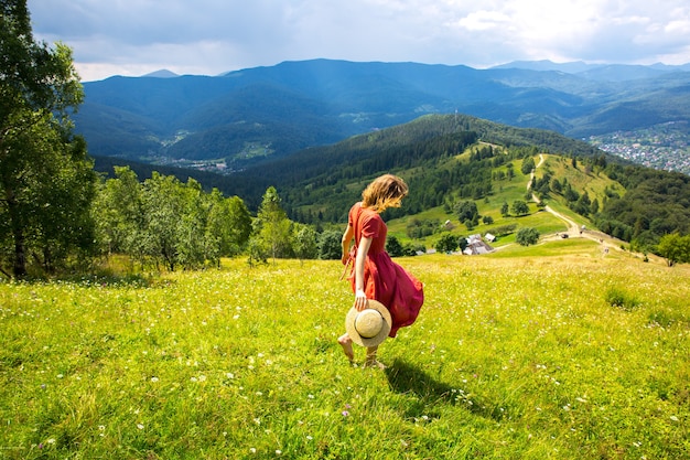 Mooi meisje de bergen. Vrouw in linnen jurk en strohoed op reis. Geweldige zomer natuur rond. Harmonie en reislust concept. Rustieke natuurlijke stijl. Wind waait voor dynamische foto.