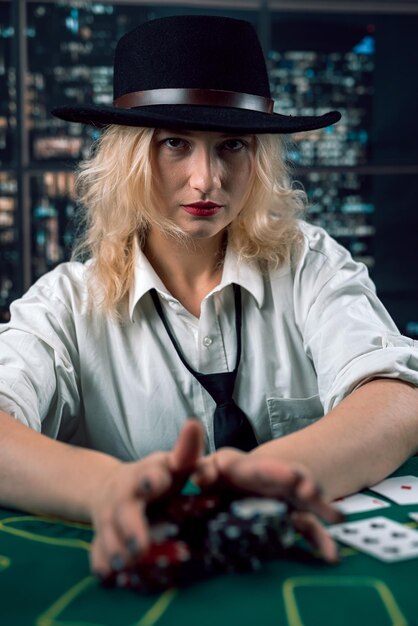 Foto mooi meisje dealer in een shirt met een zwarte stropdas deals chips aan de poker tafel de dealer kijkt naar de poker spel casino