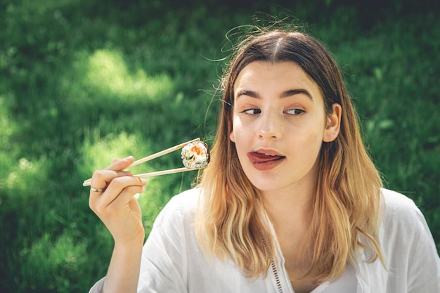 Mooi meisje eet sushi zittend op het gras in het park