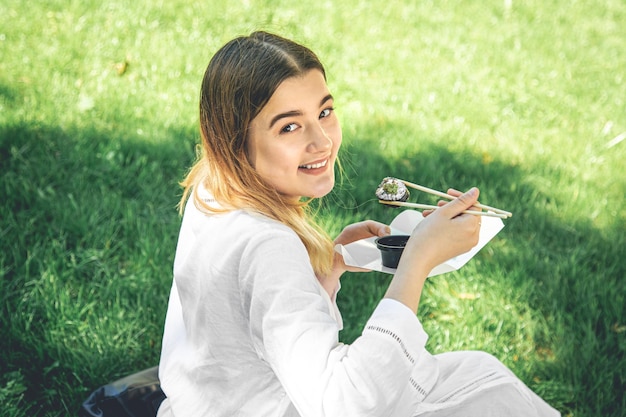 Mooi meisje eet sushi zittend op het gras in het park