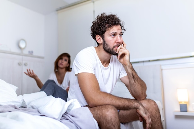 Mooi meisje en een gefrustreerde man die in bed zit en elkaar niet aankijkt. Verstoord paar dat elkaar negeert. Bezorgde man in spanning op bed. Jong koppel boos op elkaar na een gevecht.