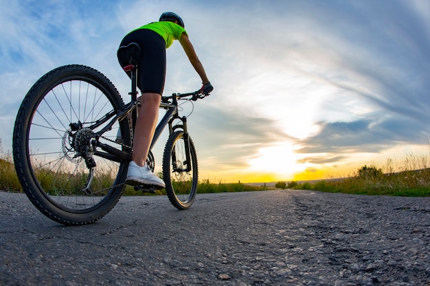 Mooi meisje fietser rijdt een fiets op de weg in de zonsondergang. Gezonde levensstijl en sport. Vrije tijd en hobby's