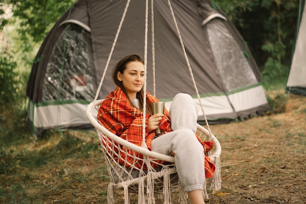 Mooi meisje gewikkeld in een rode ruit die thee drinkt in een gezellige hangstoel buiten avontuurlijke reizen