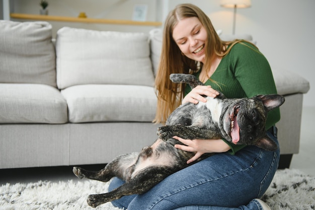 Mooi meisje glimlachend en zittend op de vloer in de buurt van Franse bulldog