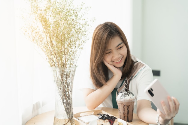 Mooi meisje glimlachend met behulp van mobiele telefoon selfie in het café, meisje eet koffie en cake