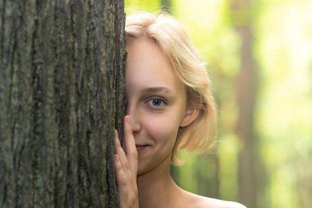 Foto mooi meisje gluren uit achter een boom in het bos