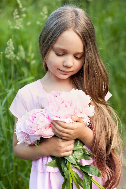 Mooi meisje houdt een roze pioenroos op een zonnige dag in de tuin.