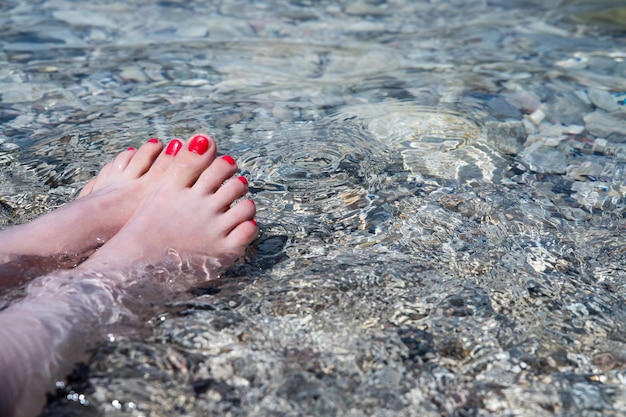 Mooi meisje houdt haar voer in het kristalheldere water op een kiezelsteenstrand in Italië