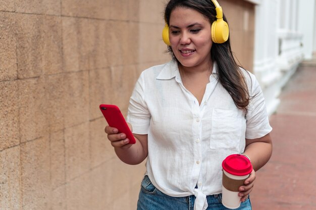 Foto mooi meisje in blouse en korte broek luisteren naar muziek en koffie drinken