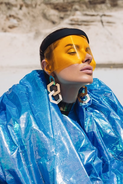 Mooi meisje in creatieve festivaloutfit, geel plastic masker en blauwe glanzende haarband