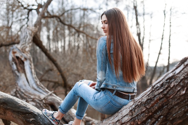 Mooi meisje in denim jasje en spijkerbroek zit op een boom en dromen