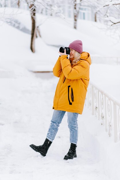 Mooi meisje in een gele jas fotograaf maakt foto's van sneeuw in een winterpark