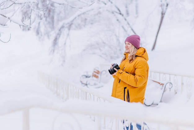 Mooi meisje in een gele jas fotograaf maakt foto's van sneeuw in een winterpark