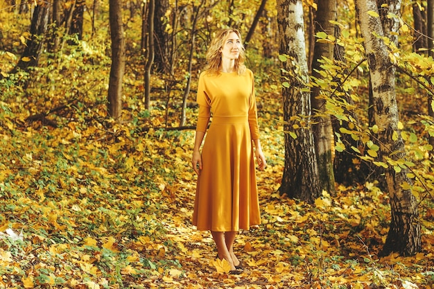 Mooi meisje in een gele lange jurk wandelingen in de herfst park met gevallen bladeren