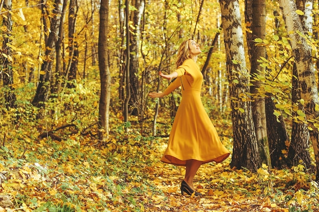 Mooi meisje in een gele lange jurk wandelingen in de herfst park met gevallen bladeren