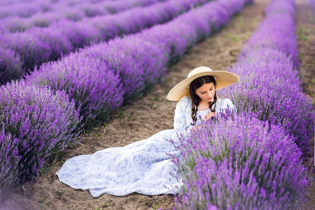 Mooi meisje in een grote hoed en een lange jurk verzamelt lavendel. Foto van de zomer.