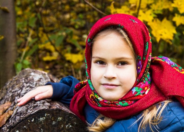 Mooi meisje in een heldere rode sjaal. portret van een meisje met bruine ogen in een oude russische sjaal op de achtergrond van de herfst. fotoshoot