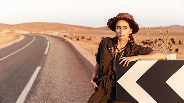 Mooi meisje in een hoed in de buurt van een verkeersbord. Op de achtergrond is een weg in de woestijn .Marokko