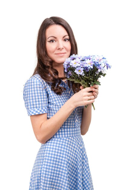 Mooi meisje in een jurk in een blauwe kooi met bloemen chrysanten in handen op een witte achtergrond