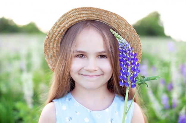 Mooi meisje in een jurk met een lupine bij zonsondergang op het veld. Het concept van natuur en romantiek. Gelukkige jeugd. Een kind houdt bloemen in de buurt van zijn gezicht. Zomer zonsondergang. Lupinus polyphyllus.