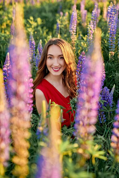 Mooi meisje in een rode jurk met een boeket lupinebloemen in het veld