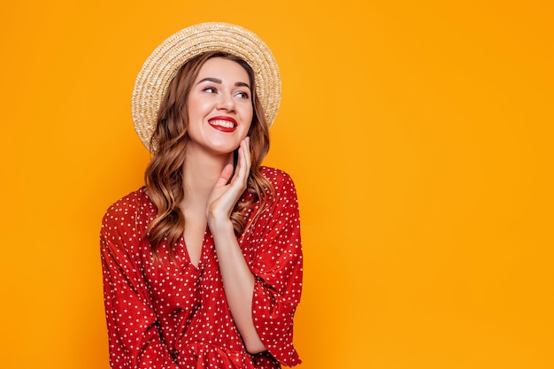 Mooi meisje in een rode kleding glimlacht dat over oranje achtergrond wordt geïsoleerd