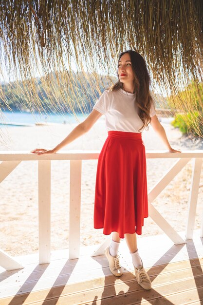 Mooi meisje in een rode rok in de zomer op een terras aan de oever van de zee Premium Foto