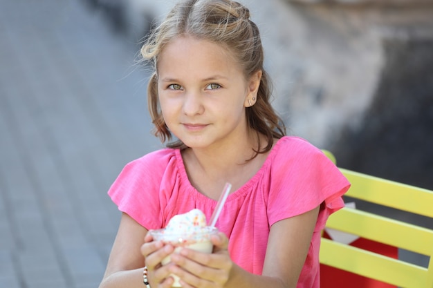 Mooi meisje in een roze t-shirt zit aan een gele tafel en eet ijs