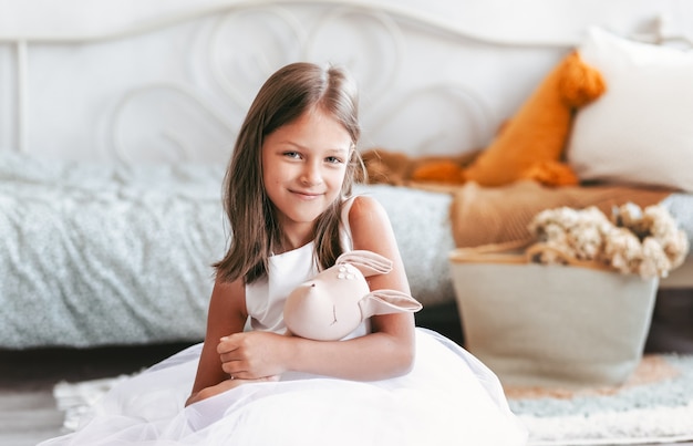 Mooi meisje in een slimme jurk speelt met een stuk speelgoed op de vloer in de kinderkamer