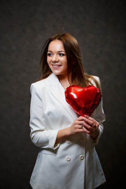 Mooi meisje in een wit jasje met een rood ballonhart in haar handen