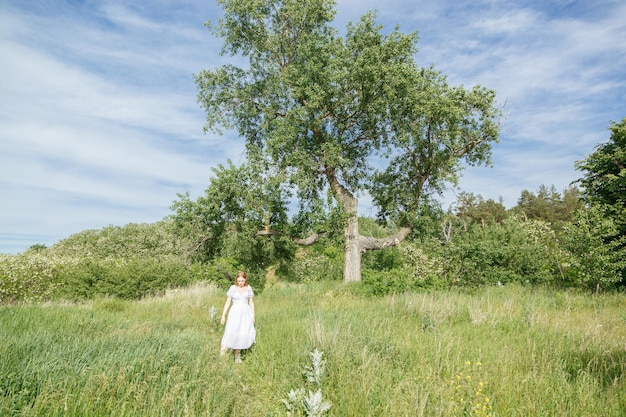 Mooi meisje in een witte jurk met bloemen in een veld met uitzicht op de lucht