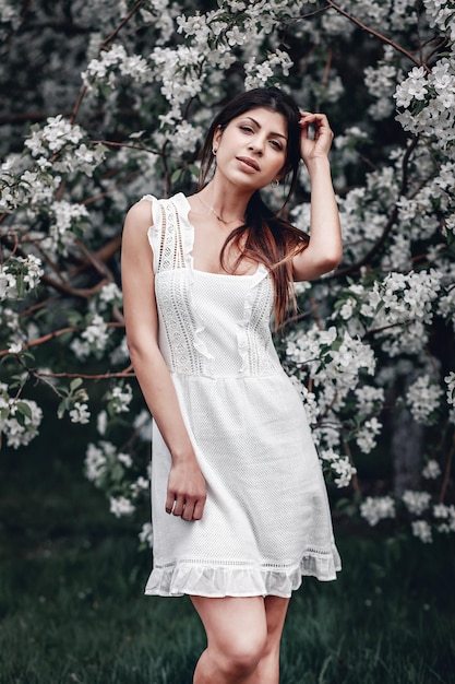 Mooi meisje in een witte jurk poseren naast een lila boom op een zonnige zomerdag, portret