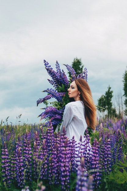 Mooi meisje in een witte jurk staande onder de lupines