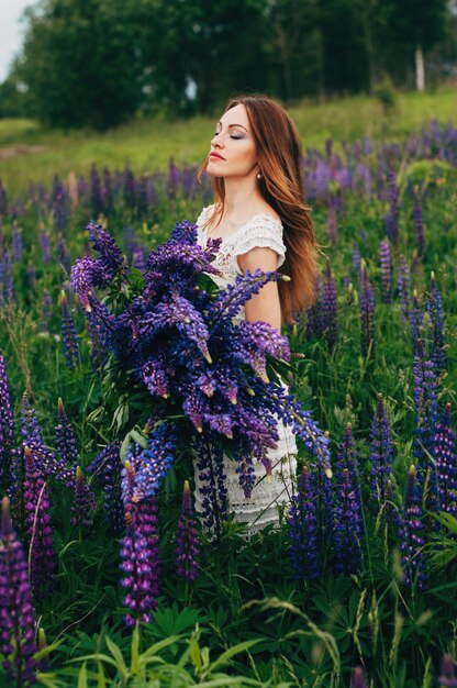 Mooi meisje in een witte jurk staande onder de lupines