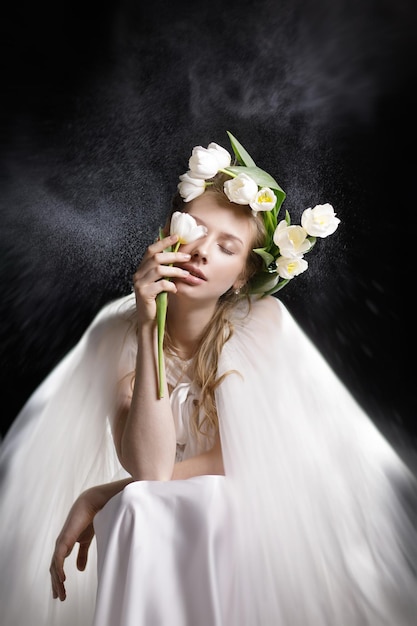 Mooi meisje in een witte trouwjurk met bloemen op haar hoofd en in haar handen