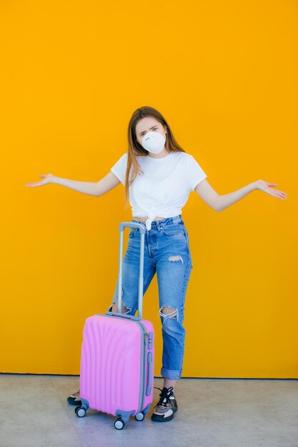 Mooi meisje in een witte zomerjurk met een koffer Medisch masker op het gezicht