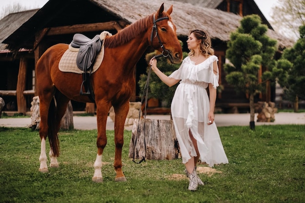 Mooi meisje in een witte zomerjurk naast een paard op een oude ranch