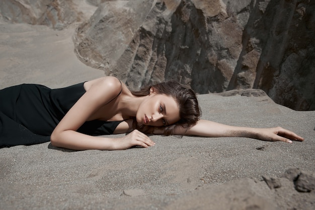 Mooi meisje in een zwarte jurk vormt in de buurt van de zandbergen