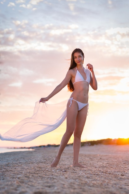 Foto mooi meisje in een zwempak op het strand bij zonsondergang