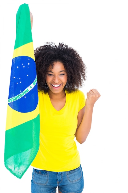 Mooi meisje in gele t-shirt die Braziliaanse vlag houden die bij camera toejuichen