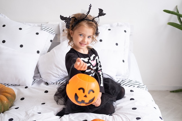 Mooi meisje in heksenkostuum met pompoen jack o lantern in ingerichte slaapkamer.